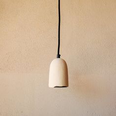 a white light hanging from a black cord on a beige wall with a brown background