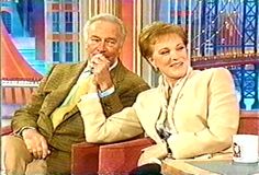 a man and woman sitting next to each other on a tv set in front of a window