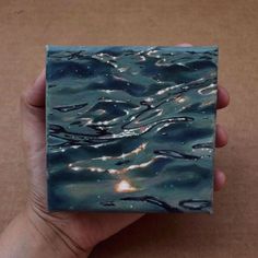 a hand holding a small square piece of paper with water and stars in the sky