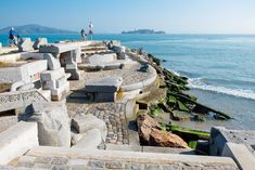 people are standing on the edge of an old stone wall overlooking the ocean and beach