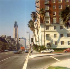 cars are driving down the street in front of tall buildings with palm trees on both sides