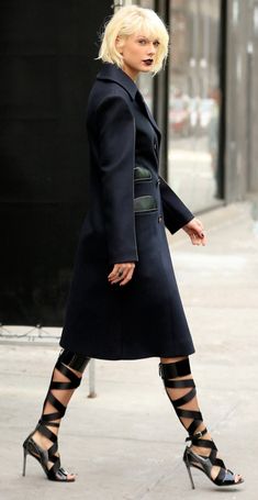 a woman walking down the street wearing high heels and a black coat with laces