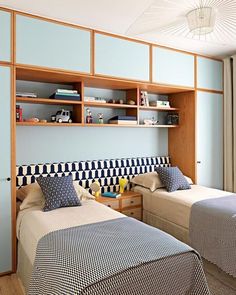 there are two beds in the room with blue and white sheets on them, one has a book shelf above it