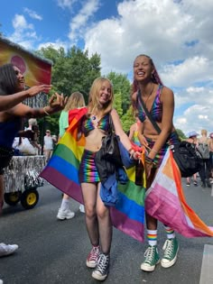 two women in rainbow outfits are walking down the street with people behind them and one is holding a flag