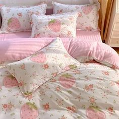 a bed covered in pink and white sheets with strawberries on them, sitting next to a night stand