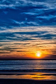 the sun is setting over the ocean with clouds in the sky