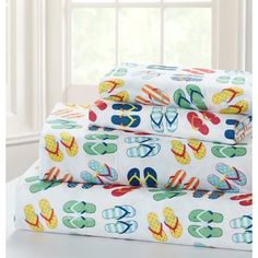 three sheets with colorful flip flops on them in front of a window and white curtains