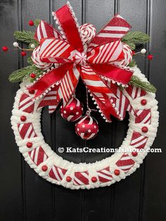 a red and white christmas wreath hanging on the front door with candy canes, bells and ornaments