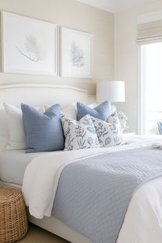 a bed with blue and white pillows on top of it next to a wicker basket