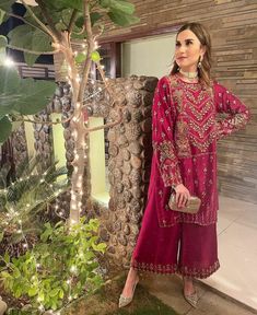 a woman standing in front of a tree wearing a pink outfit with gold details on it