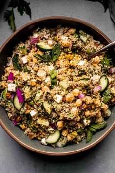 a bowl filled with vegetables and grains on top of a gray countertop next to a spoon