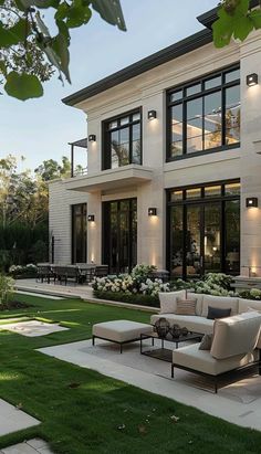 a large white house with lots of windows and furniture in the front yard, surrounded by lush green grass