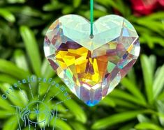 a heart shaped glass ornament hanging from a green string with flowers in the background