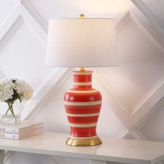 a red and white striped vase sitting on top of a table next to a lamp