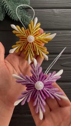 someone is holding two small ornaments in their hands, one has purple and yellow flowers on it