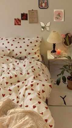 a white bed with red hearts on it in a bedroom next to a table and lamp