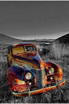 an old rusty car sitting in the middle of a field