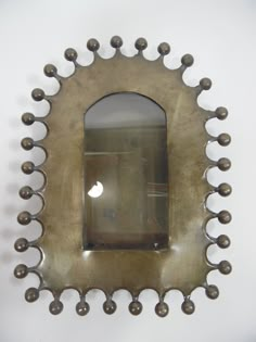 an antique mirror mounted on the wall with metal balls around it's edges and sides