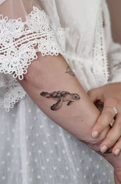 a woman with a tattoo on her arm holding onto another person's hand and wearing a white dress