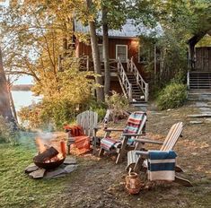 there are many lawn chairs and fire pit in front of the cabin on the lake