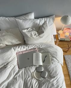 an open laptop computer sitting on top of a bed next to headphones and a book