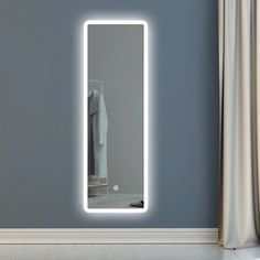 an illuminated mirror in the corner of a room with clothes hanging on a rack behind it