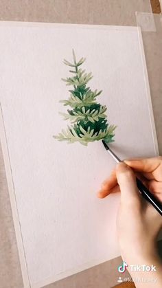 someone is painting a christmas tree with watercolors on paper and using a brush