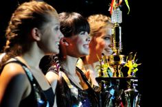 three beautiful young women standing next to each other in front of a trophy