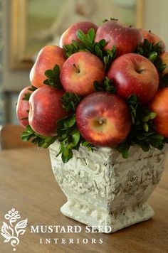 a vase filled with lots of red apples on top of a wooden table