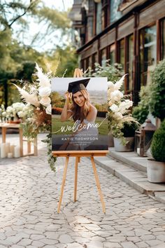 an easel with a welcome sign and flowers on it in front of a building