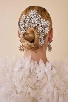 a woman wearing a white dress with flowers on her head and hair in a bun