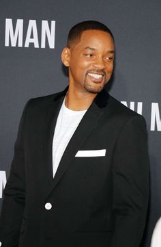 a man in a black suit smiling at the camera