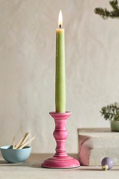 a pink candle holder sitting on top of a table next to some bowls and plants