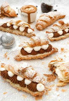 pastries are arranged on a white surface with powdered sugar and coffee in the background