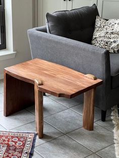 a wooden table sitting on top of a tile floor next to a gray couch and chair