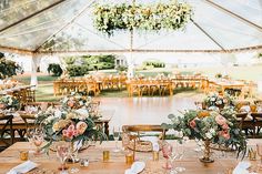 an outdoor tent set up for a wedding reception with floral centerpieces and greenery