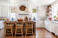 a large kitchen with white cabinets and wooden stools in the center island, surrounded by wicker bar stools