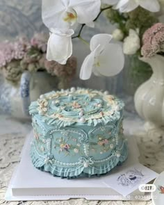 a blue cake with white flowers in the background