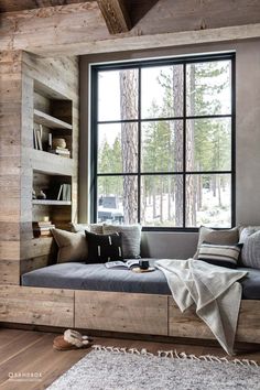 a window seat with pillows and blankets on it in front of a book shelf filled with books