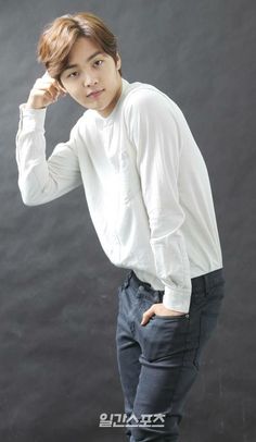 a young man poses in front of a black background with his hand on his head