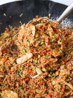 rice and vegetables being stirred in a wok with a ladle full of stir fry