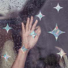 a woman is looking out the window with her hand up to some stars on it