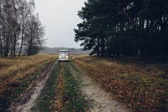 an old car driving down a dirt road in the woods