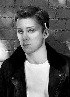 black and white photograph of a young man in front of a brick wall wearing a leather jacket