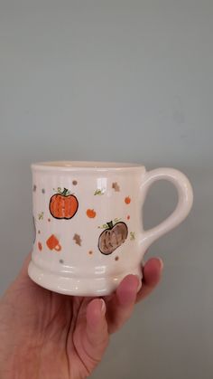 a hand holding a white coffee cup with pumpkins on it