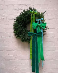 a wreath hanging on the side of a white brick wall with green ribbons tied around it