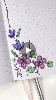 an open notebook with flowers on it and a pink ribbon hanging from the side, next to a pen