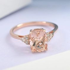 an engagement ring with a pink morganite and diamonds on the side, sitting on a white surface