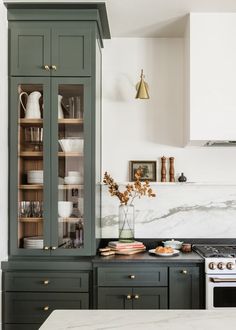 a kitchen with green cabinets and marble counter tops, gold accents on the upper cabinet