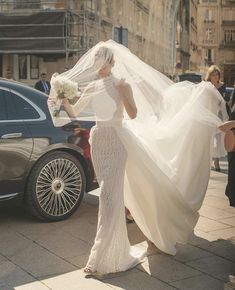 the bride is walking down the street with her veil blowing in front of her head